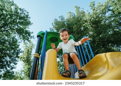 happy preschooler boy playing on a slide on the playground in summer