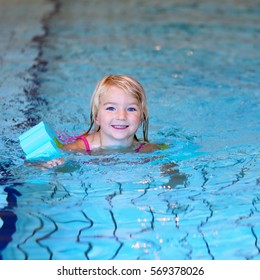 Happy Preschooler Girl Learning To Swim In Community Swimming Pool. Little Swimmer Enjoying Group Lesson At Sport School.