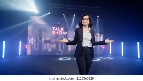 Happy presenter in a suit and glasses running onto the stage and announcing the start of the famous comedy, late-night show in an illuminated room with LED screen and 3D inscription - Shutterstock ID 2125360328