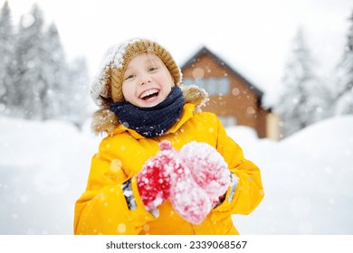 Happy preteen boy having fun playing with fresh snow during snowfall in european Alps. Child dressed in warm clothes, hat, hand gloves and scarf. Active winter outdoors leisure for children