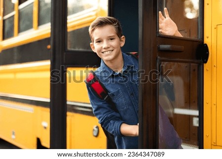 Happy preteen boy standing in door of school bus and looking at camera, cheerful male pupil wearing backpack peeking out of yellow schoolbus, ready for trip to home after lessons, copy space