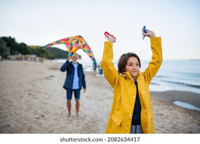 Happy preteen girl and her grandfather playing with kite on sandy beach.