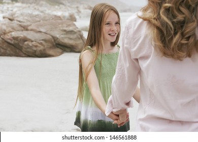 Happy Preteen Girl Looking At Mother While Playing Ring Around The Rosy On Beach