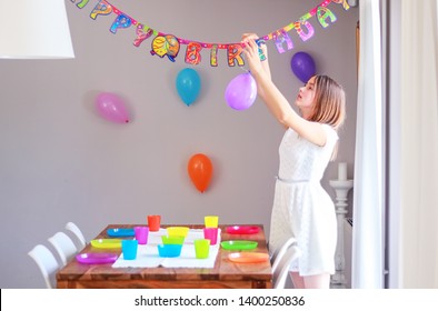 Happy preteen girl setting up table and hanging up balloons decorating house preparing to kids birthday party. Happy birthday string.