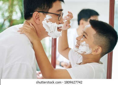 Happy preteen son putting shaving cream on nose of his father when are getting ready together in the morning - Powered by Shutterstock