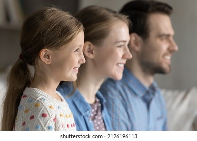 Happy Pretty 7s Girl Kid Home Portrait, Side View With Mom And Dad In Blurred Background. Family Couple Of Parents And Daughter Girl Looking Away, Smiling, Sitting In Line Together