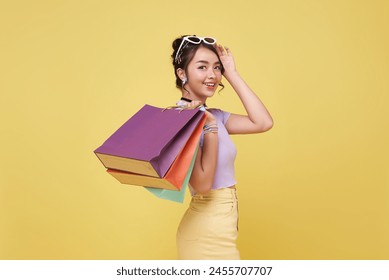Happy pretty Asian woman carrying colorful shopping bags isolated on yellow studio background.