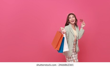 Happy pretty Asian woman carrying colorful shopping bags with credit card isolated on pink studio copy space background. - Powered by Shutterstock