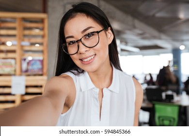 Happy Pretty Asian Young Businesswoman Standing And Taking Selfie In Office