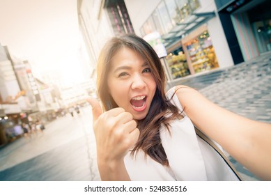 Happy pretty beautiful smiling Asian woman excited with thumb up taking selfie in city street