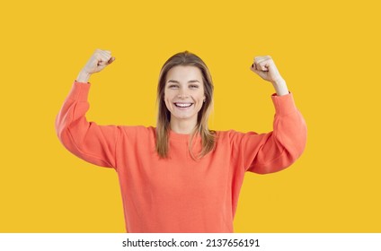 Happy Pretty Blonde Girl Demonstrating Power. Cheerful Assertive Active Energetic Young Caucasian Woman Smiling, Looking At Camera And Flexing Her Arms With Strong Bicep Muscles. Girl Power Concept