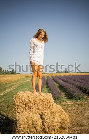 Happy pretty blonde girl in a white dress on a golden hay in the field, summer vacation