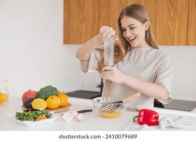 Happy pretty blonde woman in pajamas is preparing breakfast of eggs and salt it among fresh vegetables in the kitchen at home. - Powered by Shutterstock