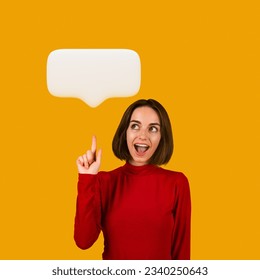 Happy pretty brunette young woman in red pointing upwards at white blank communication bubble, showing idea or share opinion and smiling, generating interesting plan. Studio shot on orange background