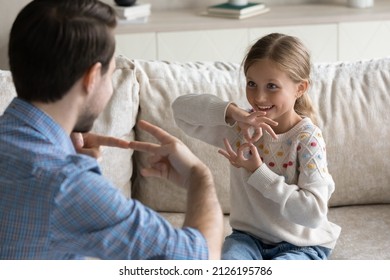 Happy Pretty Daughter Kid And Father Talking With Gestures, Speaking Sign Language At Home. Therapist Training Smiling Child With Hearing Disability, Deafness To Use Hands, Fingers For Communication