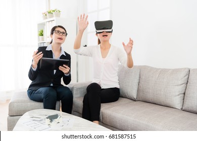 Happy Pretty Female Buyer Wearing Virtual Reality Technology Device Looking At 3D House Simulation Video And Using Hands Touching Screen Viewing All Building Construction.