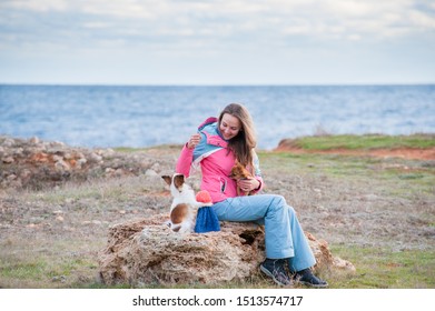 Happy Pretty Female In Track Suit Training Her Little Funny Dogs Chihuahua To Do Tricks Near Sea Shore In Spring