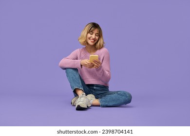 Happy pretty gen z blonde young woman model holding smartphone looking at cell texting message, smiling girl using mobile apps on cell phone sitting isolated on purple background with cellphone. - Powered by Shutterstock