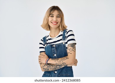 Happy pretty gen z blonde young woman, cute girl with short blond hair tattoos wearing striped t-shirt denim dress rainbow bracelet looking at camera standing isolated on white background. Portrait.