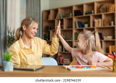 Happy Pretty Girl Giving Her Female Teacher High Five, Woman And Child Preschooler Sitting At Table Together, Learning Alphabet During Private Lesson And Celebrating Success