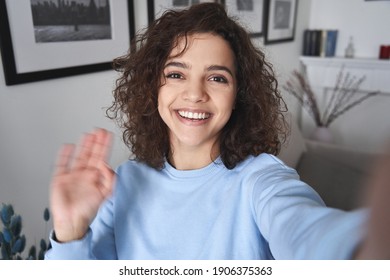 Happy Pretty Hispanic Gen Z Teen Girl Vlogger Holding Smartphone Waving Hand, Talking To Camera Shooting Vlog, Making Video Call At Home Talking By Virtual Mobile Video Call Chat App. Webcam View.