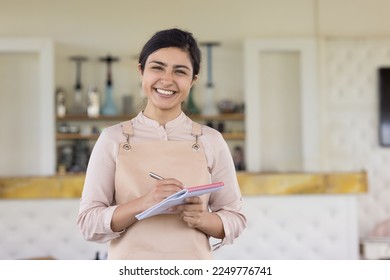 Happy pretty Indian waitress wearing apron looking at camera, smiling. Female entrepreneur, businesswoman, small business owner, hookah lounge, eastern coffee shop, tea house manager portrait - Powered by Shutterstock