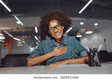 Happy Pretty Lady Sitting At Work Desk And Showing Gestures In Modern Office