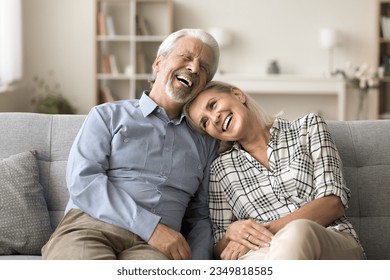 Happy pretty mature wife resting on sofa with head on husbands shoulder. Senior family couple relaxing on couch together, talking, discussing vacation, smiling, laughing - Powered by Shutterstock