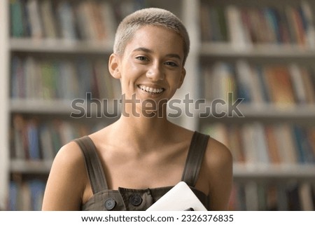 Happy pretty stylish short haired student girl with teeth brackets standing in campus library, looking at camera, smiling, laughing, showing braces. Head shot portrait