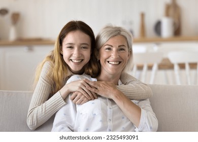 Happy pretty teenage grandkid girl and positive blonde grandmother head shot home portrait. Teen child hugging mature mom from behind, looking at camera with toothy smile, laughing - Powered by Shutterstock