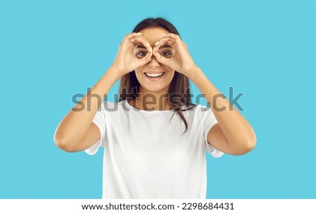 Happy pretty woman looking through pretend binoculars. Cheerful beautiful young brunette lady in white T shirt forming circles with her hands, doing binoculars gesture, looking in distance and smiling