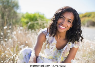 Happy pretty woman sitting on the grass in floral dress on a sunny day in the countryside - Powered by Shutterstock