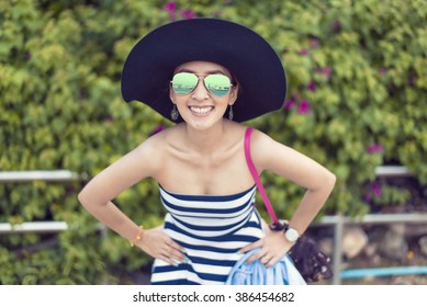 happy pretty woman smiling in the beach wearing a Black and white striped dress with the sea and green in the background