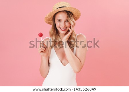 Happy pretty young girl wearing swimsuit standing isolated over pink background, holding lollipop