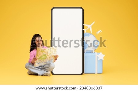 Happy pretty young lady in casual sitting on floor, holding map, planning vacation, sitting by big phone with white blank screen, yellow background, mockup, collage. Travelling, tourism, journey