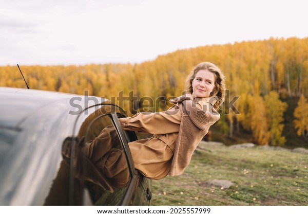 A happy pretty young woman in\
casual clothes enjoys solitude drinking coffee walking traveling by\
car in the autumn forest in nature in fall, selective\
focus