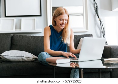 Happy Pretty Young Woman Sitting On Sofa And Using Laptop At Home