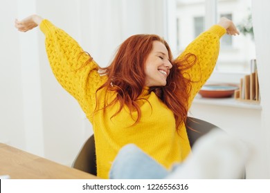 Happy pretty young woman stretching her arms as she leans back relaxing in her chair with a beaming smile