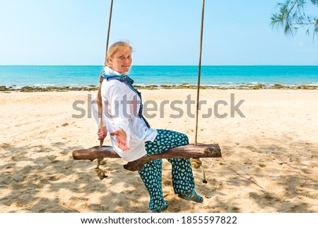 Happy pretty young woman swinging on beach swing at tropical island