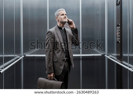 Happy priest standing in the elevator and having a phone call with his smartphone
