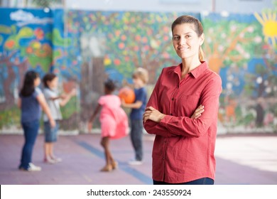 Happy Primary School Teacher With Her Students Playing In Schoolyard.