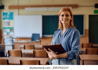 Happy primary school teacher standing in the classroom and looking at camera. - Powered by Shutterstock