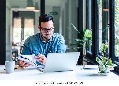 Happy professional analyzing business ideas in diary at table. Businessman making success plan while working on laptop. He is wearing casuals in home office or business office. - Powered by Shutterstock