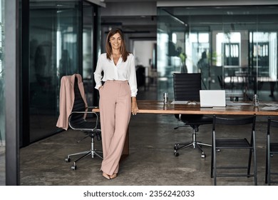 Happy professional elegant mature 45 years old business woman, smiling Latin businesswoman executive manager leader, middle aged female entrepreneur standing at work in office. Full body portrait. - Powered by Shutterstock