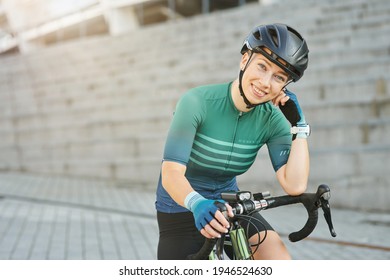 Happy professional female cyclist in protective gear smiling at camera while standing with her bike outdoors on a daytime - Powered by Shutterstock