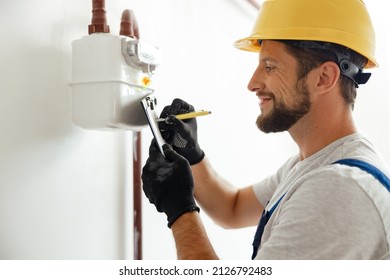 Happy Professional Heating Fitter Making Notes While Checking Gas Consumption At Gas Pipe And Meter Counter