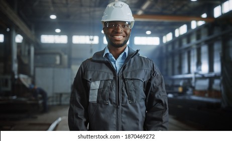 Happy Professional Heavy Industry Engineer Worker Wearing Uniform, Glasses and Hard Hat in a Steel Factory. Smiling African American Industrial Specialist Standing in a Metal Construction Manufacture. - Shutterstock ID 1870469272