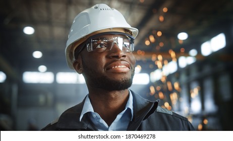 Happy Professional Heavy Industry Engineer Worker Wearing Uniform, Glasses and Hard Hat in a Steel Factory. Smiling African American Industrial Specialist Standing in a Metal Construction Manufacture. - Shutterstock ID 1870469278