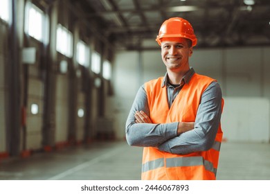 Happy, professional man, foreman, builder wearing workwear and hard hat, looking at camera with crossed arms, copy space in warehouse. Concept of industry, advertisement - Powered by Shutterstock