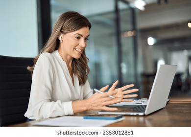 Happy professional mature female hr manager, smiling mature mid aged business woman in office wearing earbud looking at laptop computer having hybrid conference work meeting or remote job interview. - Powered by Shutterstock